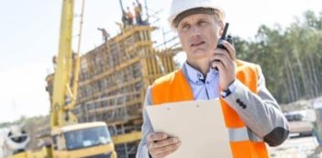Supervisor using walkie-talkie while holding clipboard at construction site